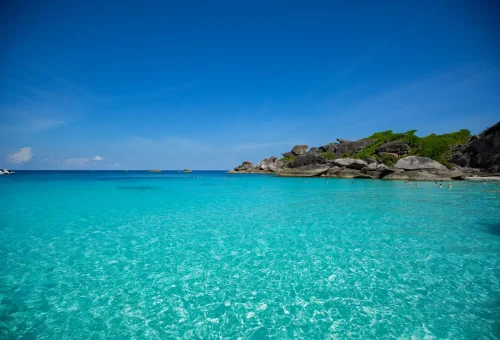 Clear shallow waters of Similan Islands with visible coral reef and swimmers, Thailand.