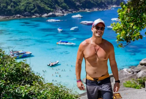Smiling tourist enjoying Similan Islands viewpoint with crystal-clear blue sea and boats in the background, Phuket, Thailand.