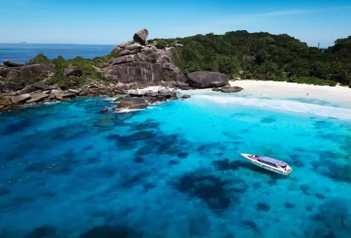Speedboat floating in crystal-clear waters near Similan Islands white sand beach.