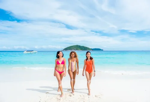 Three women walking on white sandy beach with turquoise sea at Similan Islands.
