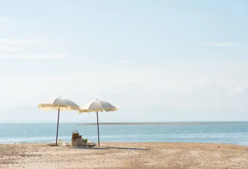 Shaded beach umbrellas on white sand with picnic basket on Pah Island.