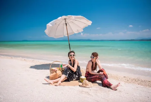 Two women sunbathing under umbrellas on the pristine Pah Island sandbank.