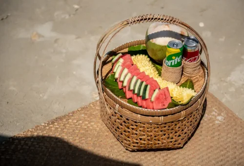 Traditional Thai picnic basket with tropical fruits, coconut, and soft drinks on Pah Island beach.