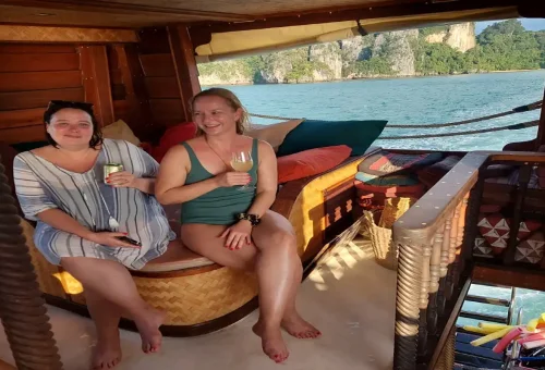 Two women relaxing with drinks inside the boat lounge overlooking Phang Nga Bay.
