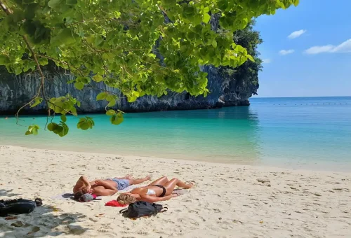 Couple sunbathing on quiet sandy beach with turquoise waters at Hong Island Krabi.