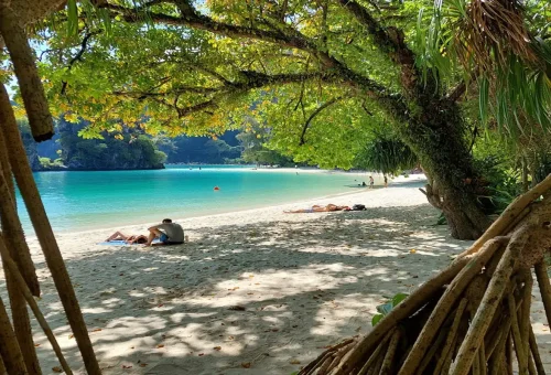 Tourists relaxing on shaded beach at Koh Hong Krabi with emerald green water.