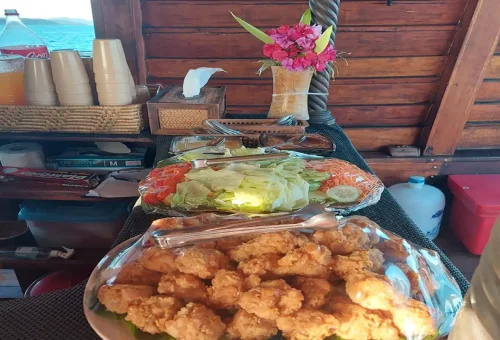 Buffet table with fried chicken, salad, and tropical drinks prepared on cruise boat.