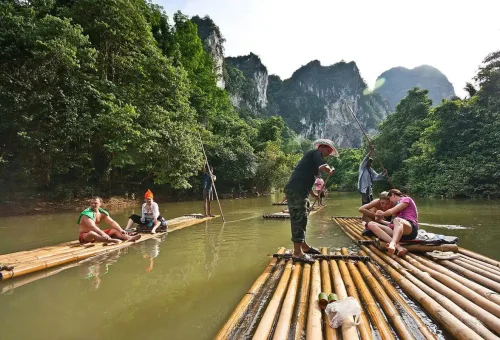 Travelers on bamboo rafts floating through Khao Sok National Park’s limestone cliffs.