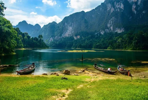 Longtail boats docked on Cheow Lan Lake surrounded by jungle mountains.