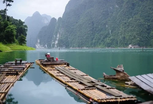 Bamboo rafts floating on emerald Cheow Lan Lake with limestone cliffs in the background.