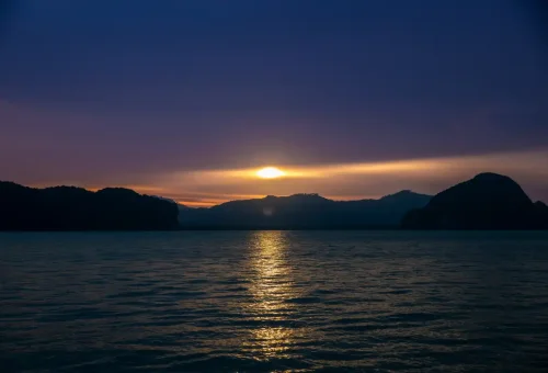 Golden sunset over Phang Nga Bay limestone mountains during the Sunset Serenity Cruise by Phuket Travel Store.