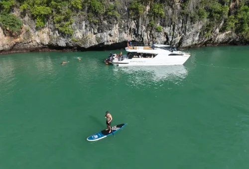 Traveler paddleboarding beside luxury catamaran yacht on Phang Nga Bay Sunset Serenity Cruise with Phuket Travel Store.