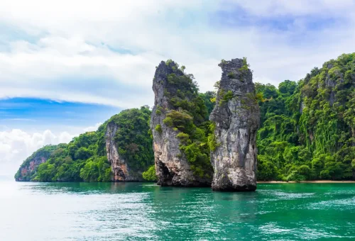 Majestic limestone cliffs and lush green jungle rising from turquoise waters in Phang Nga Bay with Phuket Travel Store.