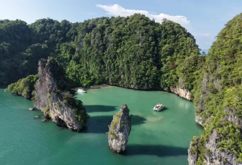 Luxury yacht anchored in emerald lagoon surrounded by towering limestone cliffs on Phang Nga Bay Sunset Cruise with Phuket Travel Store.