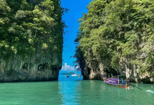 Longtail boat sailing through limestone cliffs at Hong Island, Krabi.