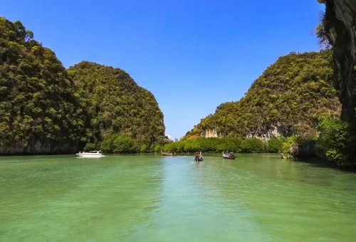 Longtail boats anchored in emerald lagoon surrounded by cliffs at Hong Island.
