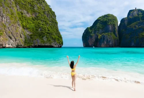 Happy traveler raising arms on the beach at Maya Bay, Phi Phi Islands.