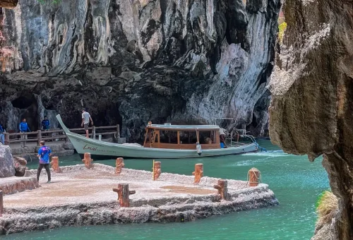 Traditional longtail boat docking near limestone cave in Phang Nga Bay