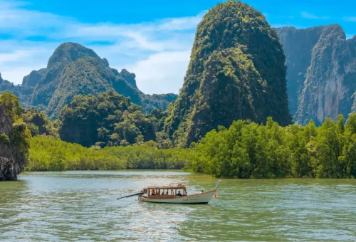 Private longtail boat cruising through mangroves and limestone cliffs in Phang Nga Bay Thailand