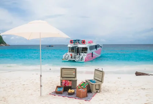 Luxury speedboat anchored at Raya Noi Island beach with picnic setup under white umbrella by Phuket Travel Store