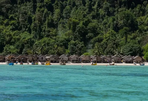 Moken village huts along the beach surrounded by lush jungle on Surin Islands Thailand.