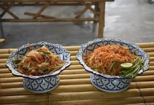 Traditional Thai ingredients like bean sprouts, tofu, and chives arranged in blue ceramic bowls