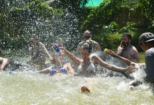Tourists splashing water and laughing while bathing elephants in a natural pond at Phuket Elephant Care Park.