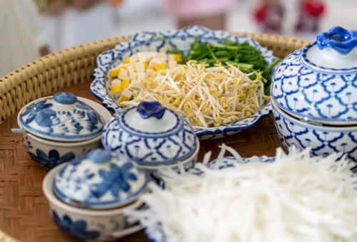 Traditional Thai dishes including papaya salad and fried noodles served in patterned blue bowls.
