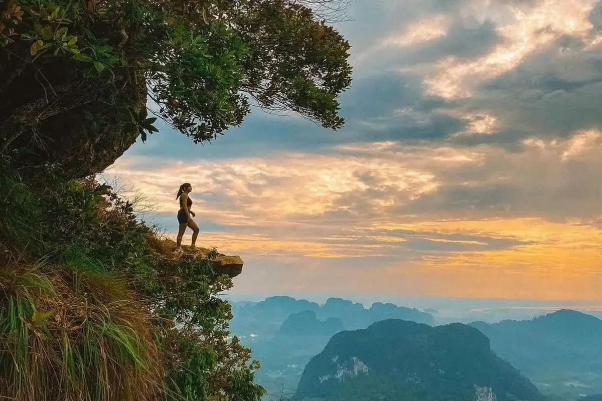 Adventurer standing on cliff edge at sunrise overlooking limestone mountains in Krabi, Thailand, symbolizing freedom and exploration.