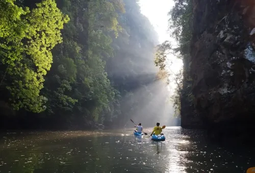 Kayakers paddling under sunlight beams in limestone canyon Ao Thalane Krabi