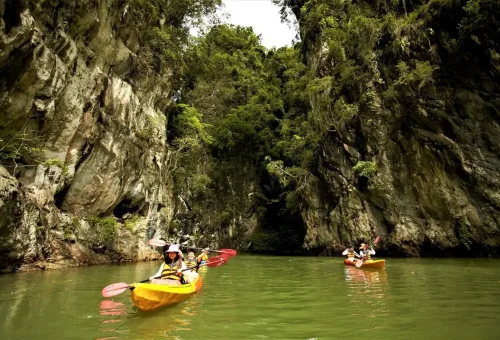 Kayakers in orange boats entering a lagoon between limestone cliffs in Ao Thalane, Krabi.