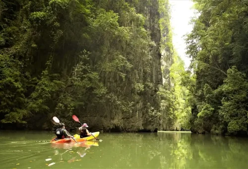 Kayakers paddling through narrow canyon surrounded by tall limestone cliffs in Ao Thalane.