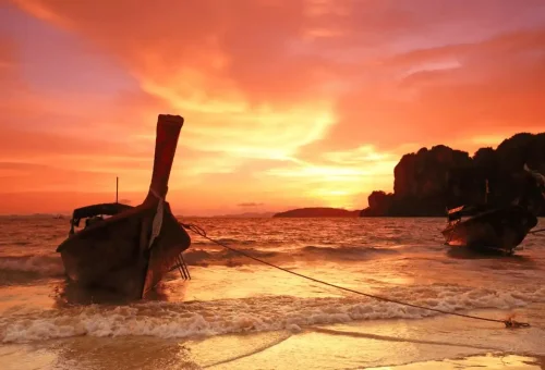 Traditional longtail boats at Railay Beach during a vibrant red-orange sunset in Krabi