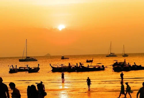 Sunset with longtail boats and tourists enjoying BBQ dinner on the beach in Krabi