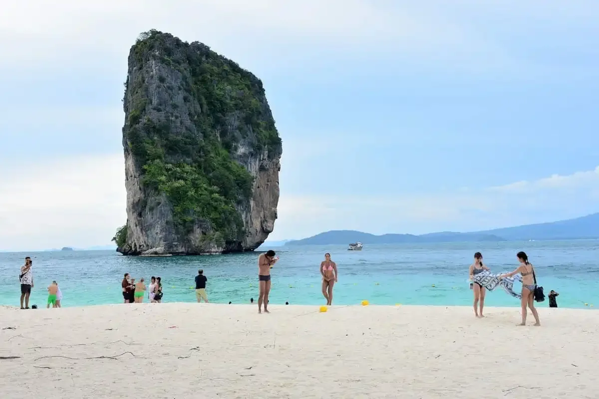 Visitors relaxing and swimming at Koh Poda Island with limestone cliffs in Krabi.