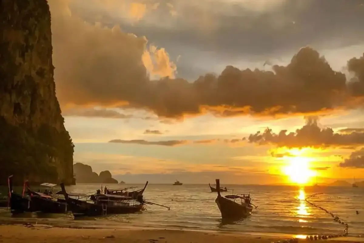 Sunset over Railay Beach with traditional longtail boats anchored in the sea.