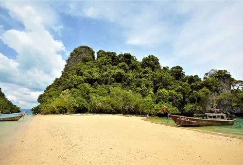 Longtail boats anchored at a sandy beach near limestone cliffs during the James Bond Island tour from Krabi.