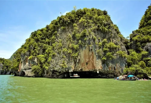 Limestone cave with tour boats entering through the cave mouth in Phang Nga Bay.
