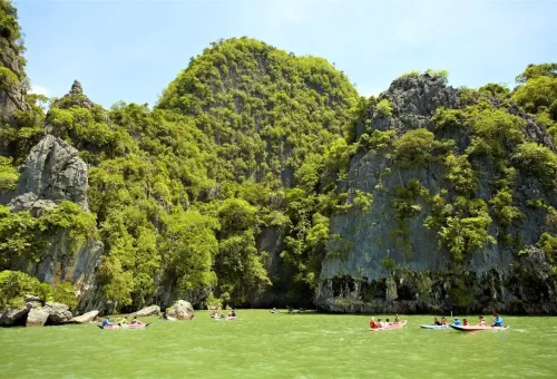 Tourists canoeing between towering limestone cliffs covered in lush tropical greenery.