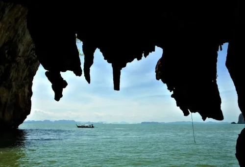 Longtail boat seen through stalactites hanging at the entrance of a sea cave in Phang Nga Bay.