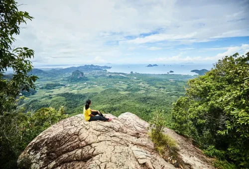 Hiker resting on the summit of Dragon Crest Mountain overlooking Krabi’s lush valley and Andaman Sea.