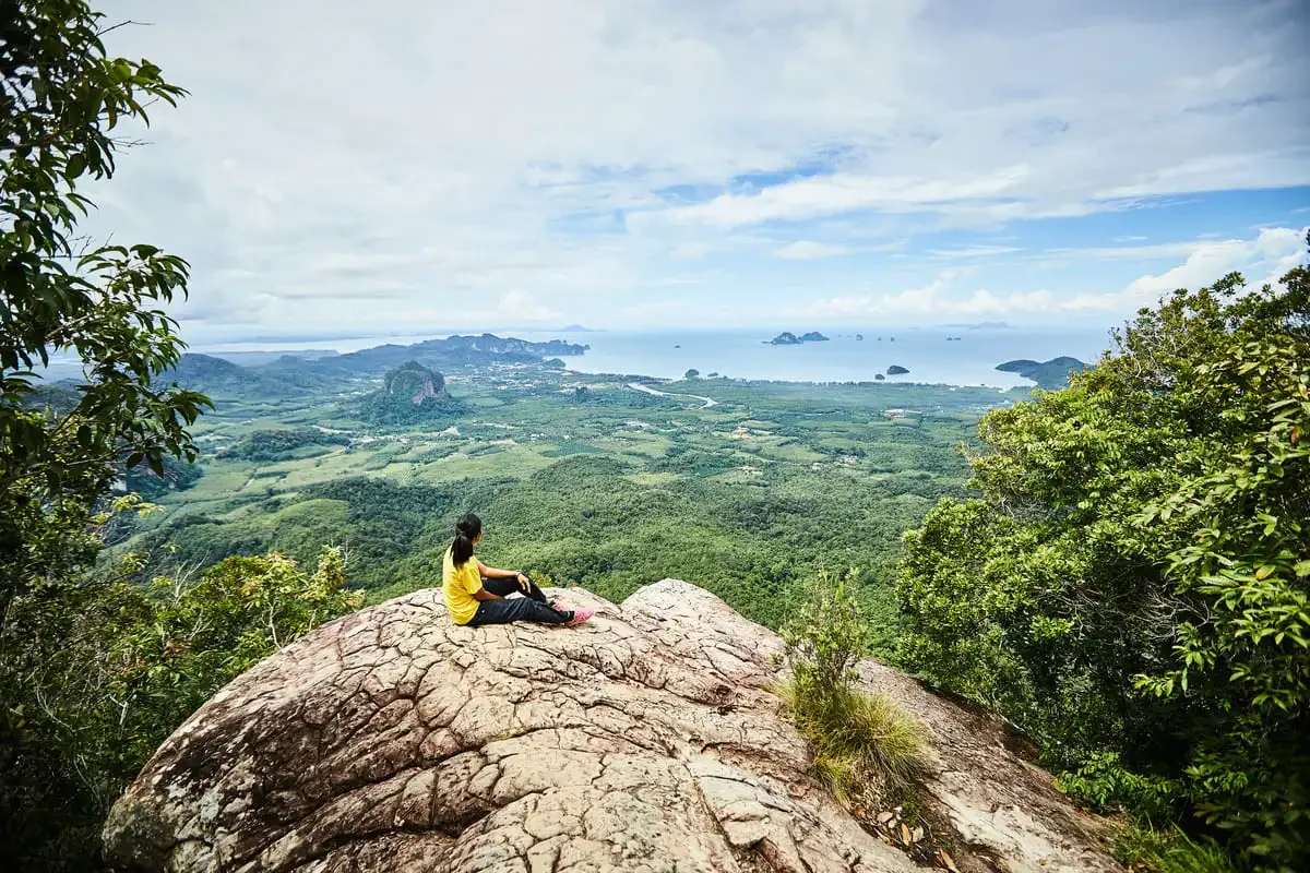 Hiker resting on the summit of Dragon Crest Mountain overlooking Krabi’s lush valley and Andaman Sea.