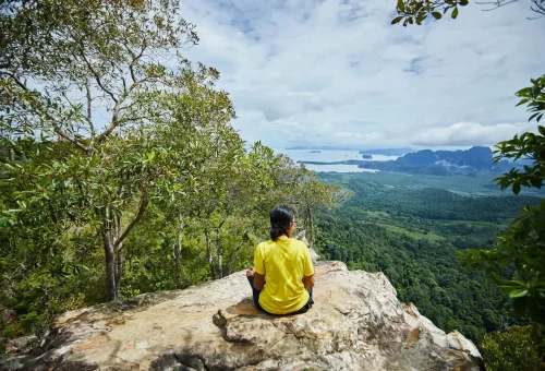 Woman sitting on a cliff edge enjoying panoramic sea and forest views from Dragon Crest Mountain.