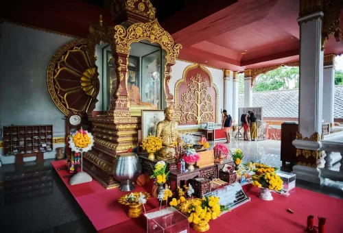 Golden monk shrine inside a Thai temple on Koh Samui with flowers and offerings during the Koh Samui Explorer Tour.