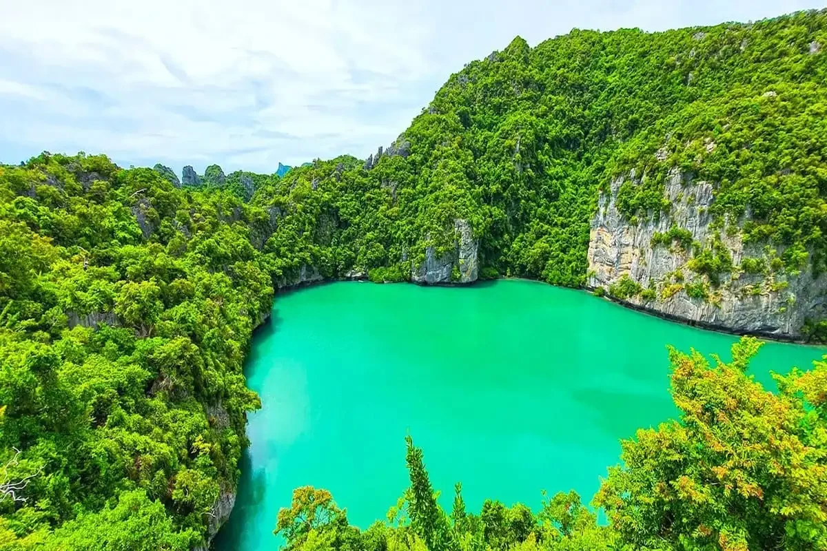 Emerald Lagoon at Angthong Marine Park surrounded by lush green cliffs and tropical forest in the Gulf of Thailand.