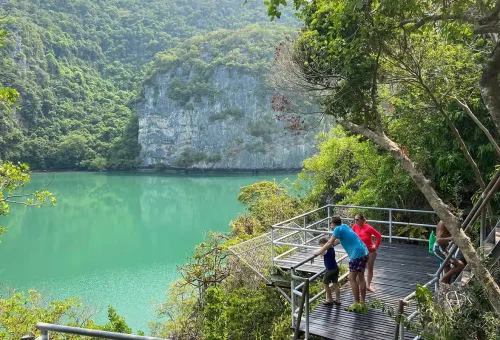 Tourists viewing the green Emerald Lagoon surrounded by steep limestone cliffs at Angthong Marine Park.