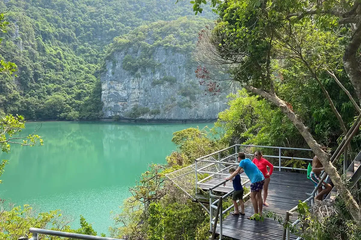 Tourists viewing the green Emerald Lagoon surrounded by steep limestone cliffs at Angthong Marine Park.