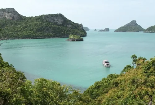Boat cruising through turquoise waters and limestone islands of Angthong Marine Park.