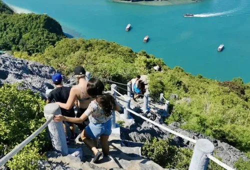 Tourists descending the steep trail overlooking turquoise water and boats in Angthong Marine Park.