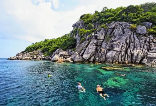 Travelers snorkeling near limestone cliffs and coral reefs at Angthong Marine Park.